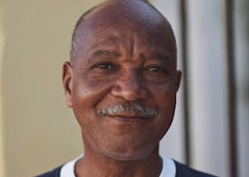 Home A joyful portrait of an elderly African man with a mustache, enjoying the sunlight.